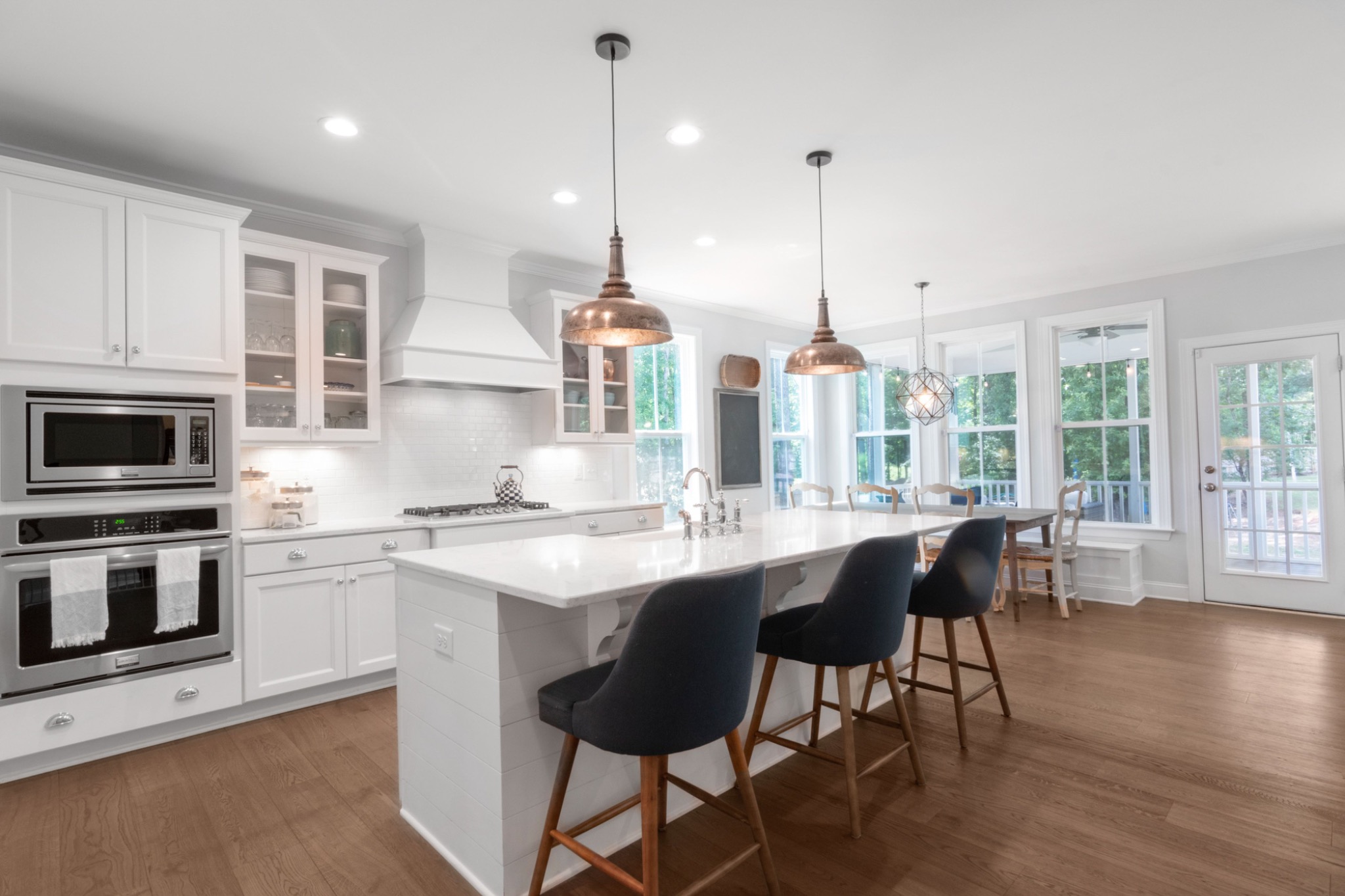 Bright white kitchen with copper pendant lights and dark upholstered barstools; illustrative Pexels photography